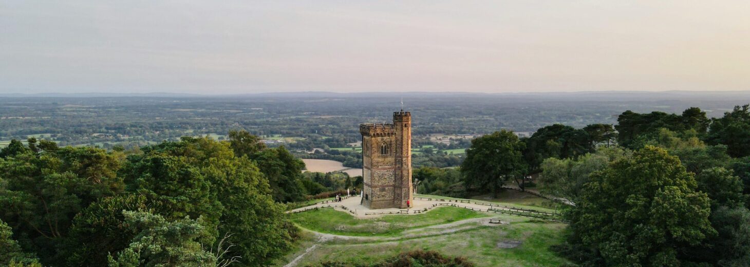 This picutre shows a gothic medieval tower on green hill under a sundown sky.